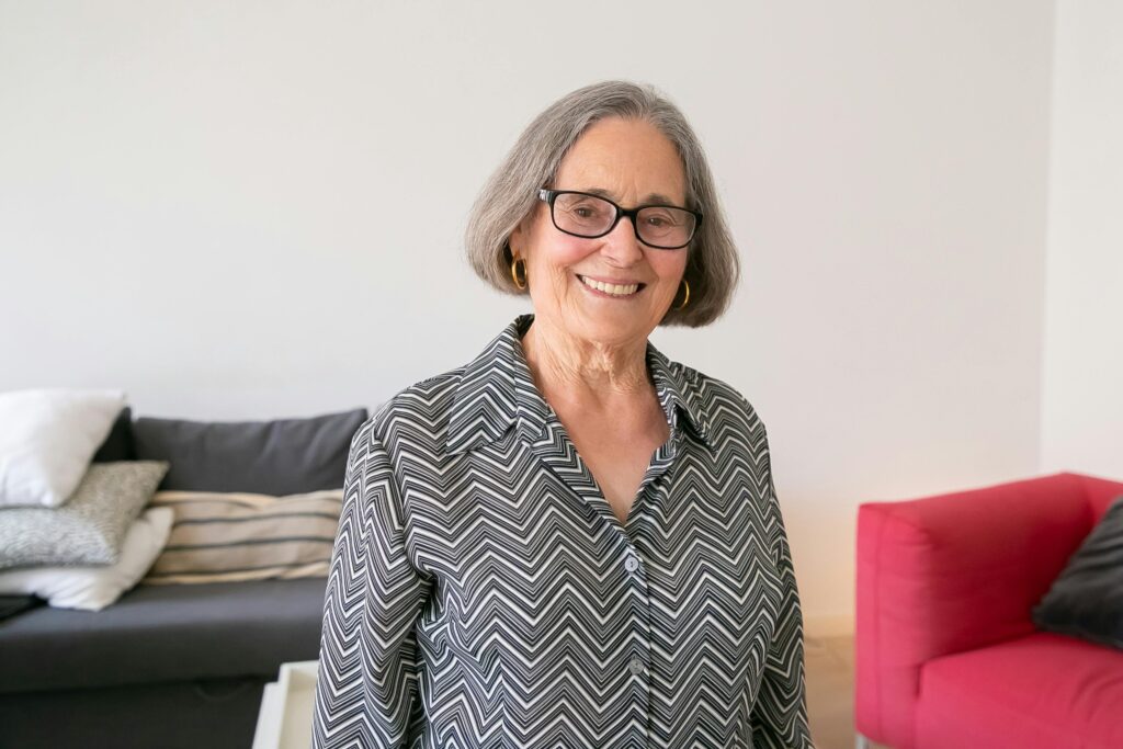 Charming senior woman with eyeglasses smiling warmly at home in a relaxed indoor setting.