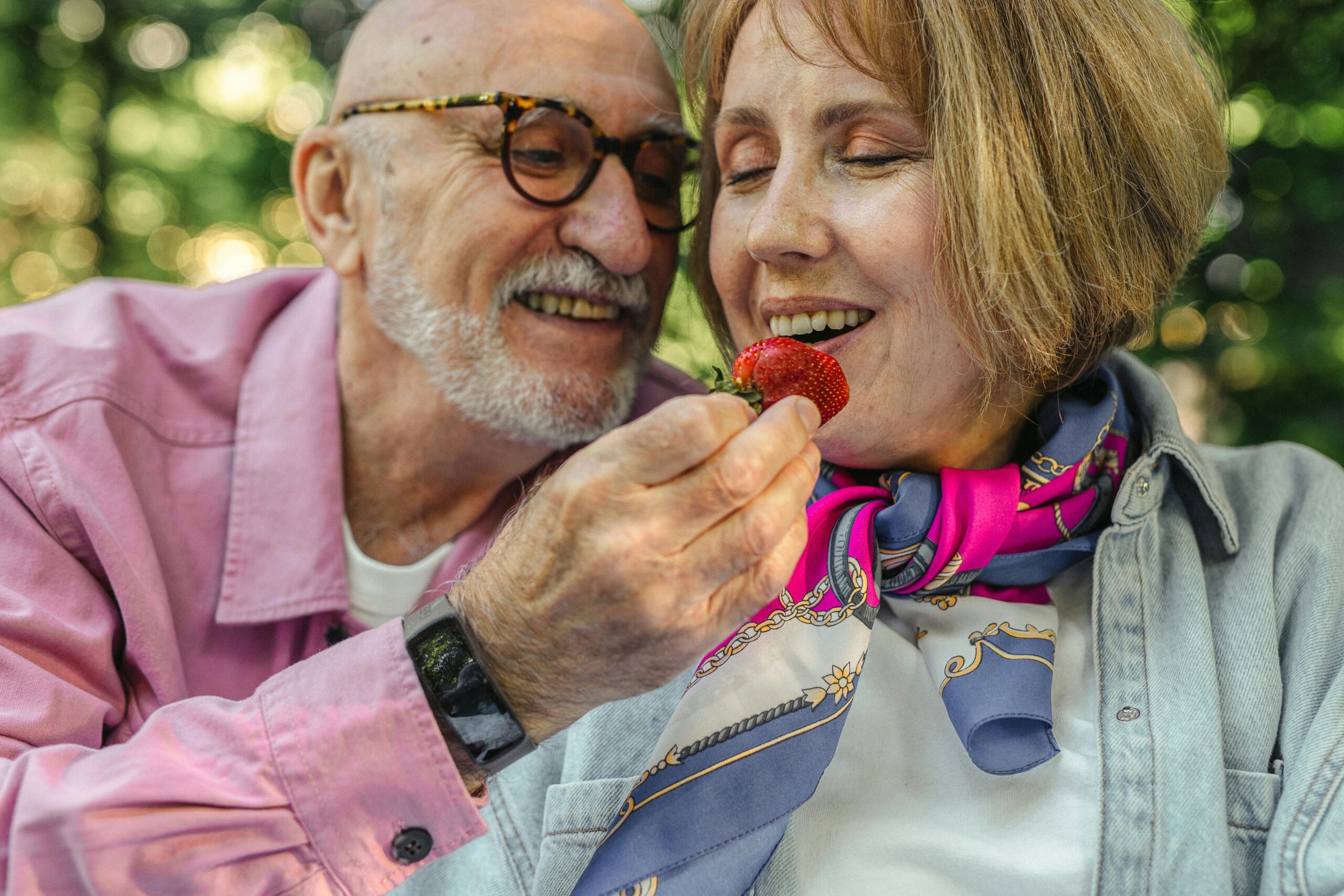 Charming senior couple enjoying a strawberry together outdoors in a romantic setting.
