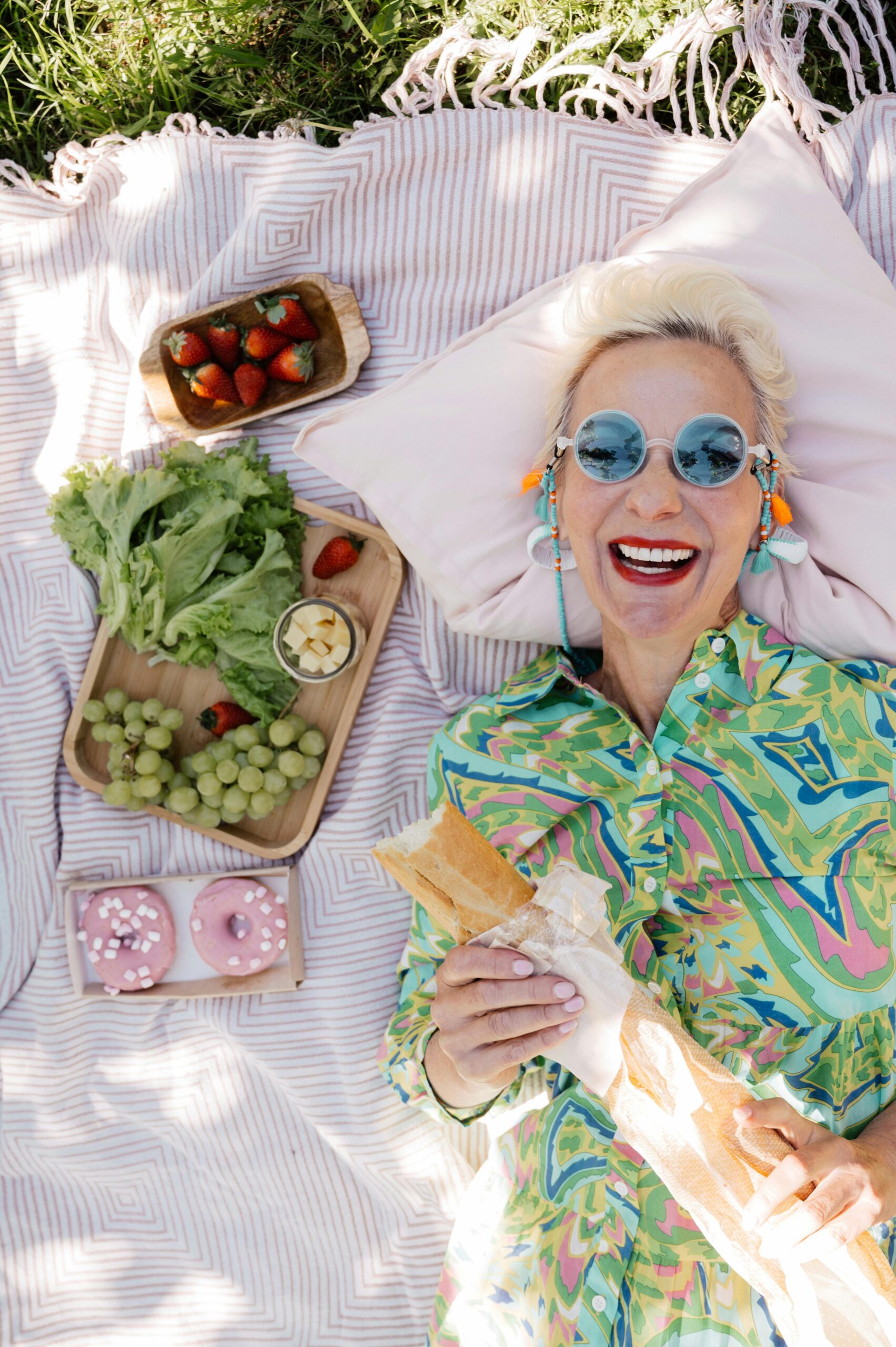2 Senior woman with pastries and salad at a sunny picnic, smiling joyfully.